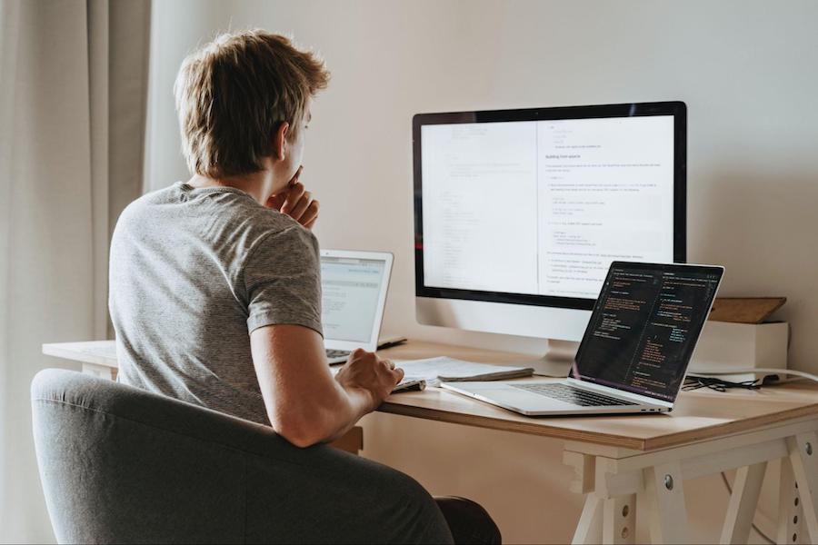 man sits at desk in front of three computers project scope - project deliverables
